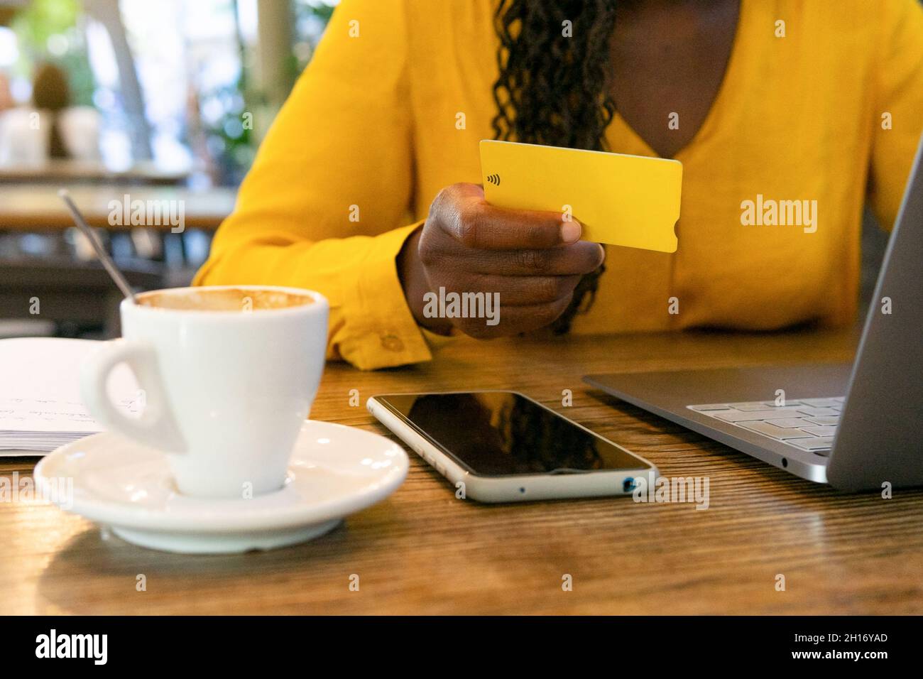 Anonyme afroamerikanische Freiberuflerin mit Kreditkarte, die mit Netbook am Tisch sitzt, während sie Online-Einkäufe auf der Terrasse im Café täte Stockfoto