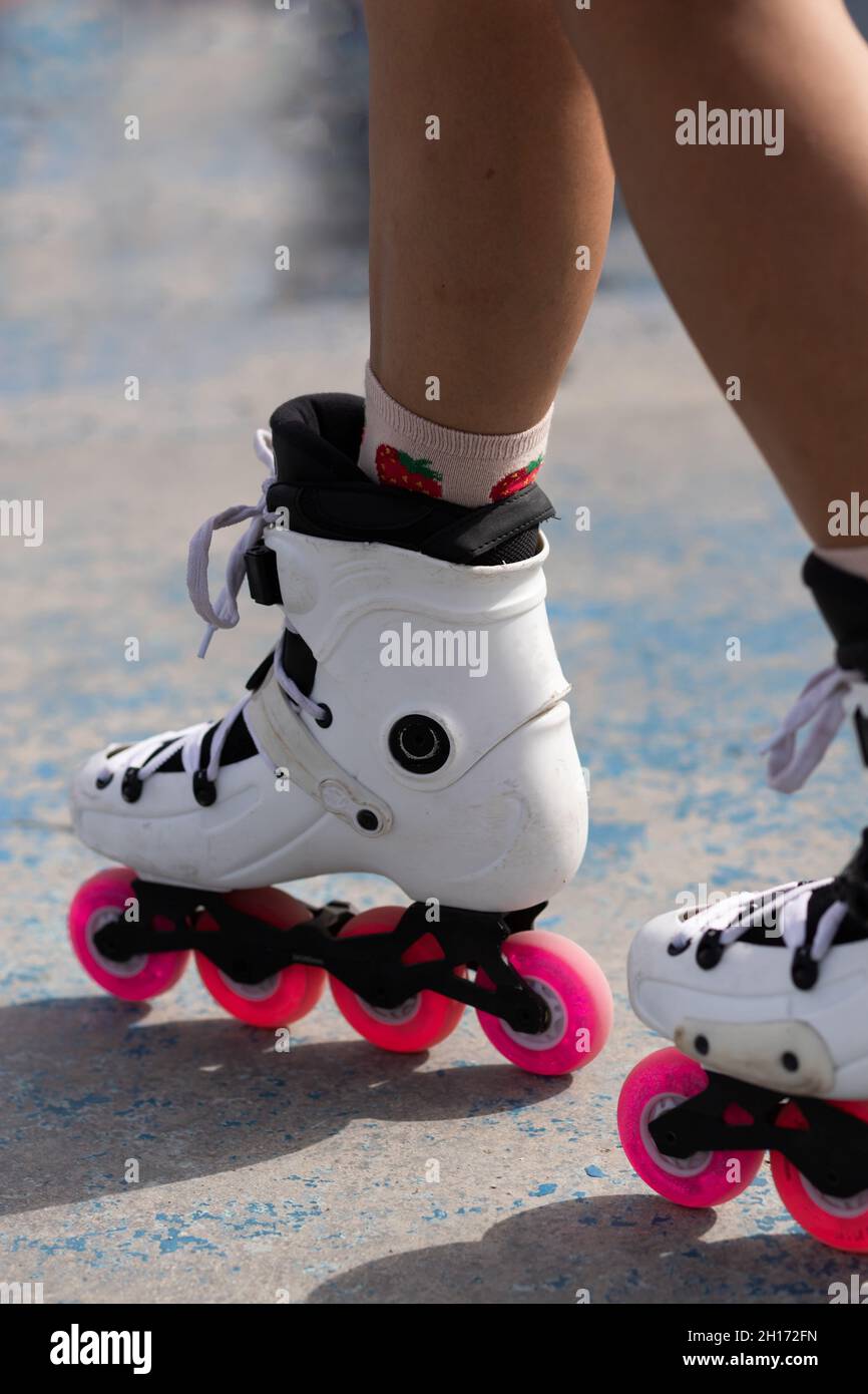 Beschneiden Sie anonyme weibliche Beine in weißen Rollern mit pinken Rädern, die auf Betonpflaster im Skatepark stehen Stockfoto