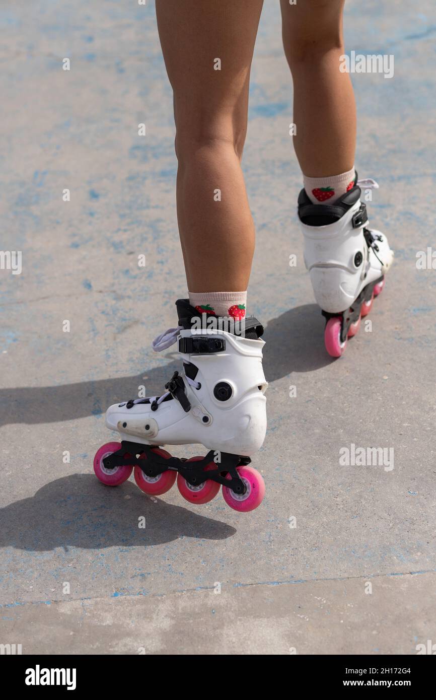 Beschneiden Sie anonyme weibliche Beine in weißen Rollern mit pinken Rädern, die auf Betonpflaster im Skatepark stehen Stockfoto
