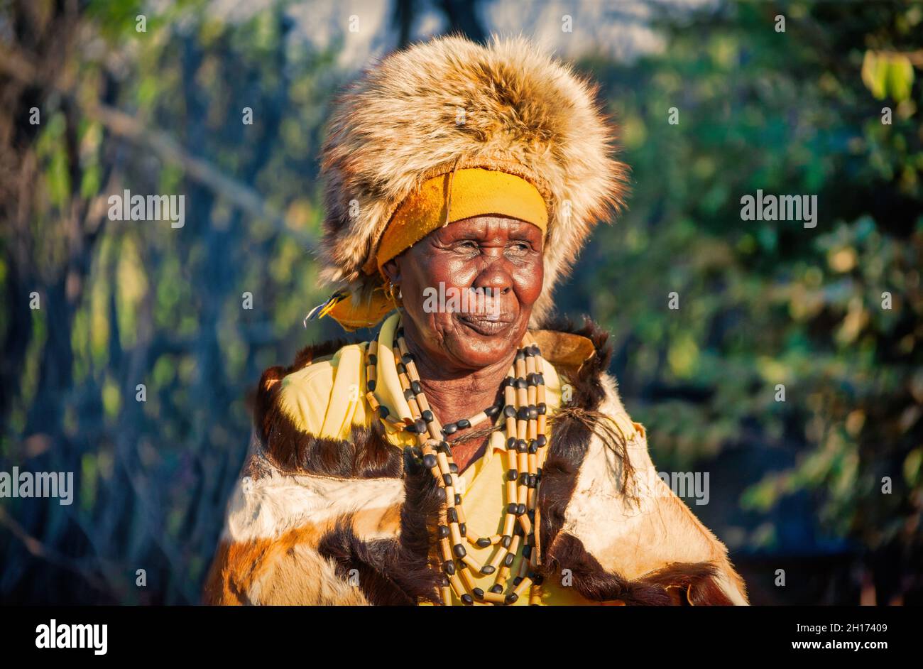 Zwei ältere Frauen aus dem südlichen Afrika, die in einer traditionellen Tracht mit Hut und Kuh gekleidet sind, verstecken sich in einem Dorf auf dem Land Stockfoto