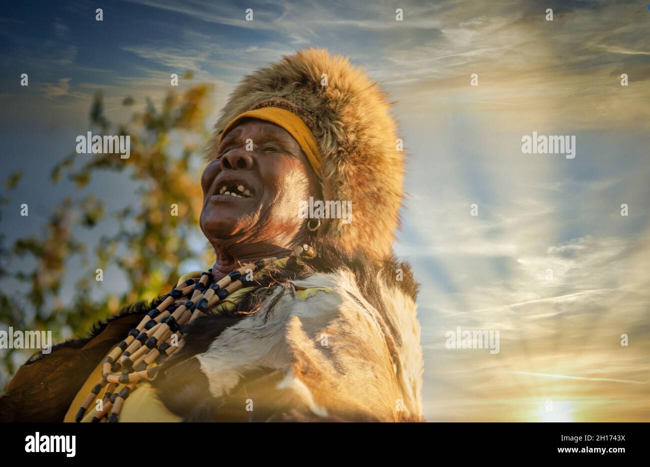 Die ältere Frau aus dem südlichen Afrika, die in einer traditionellen Tracht mit Hut und Kuh gekleidet ist, versteckt sich in einem Dorf auf dem Land Stockfoto