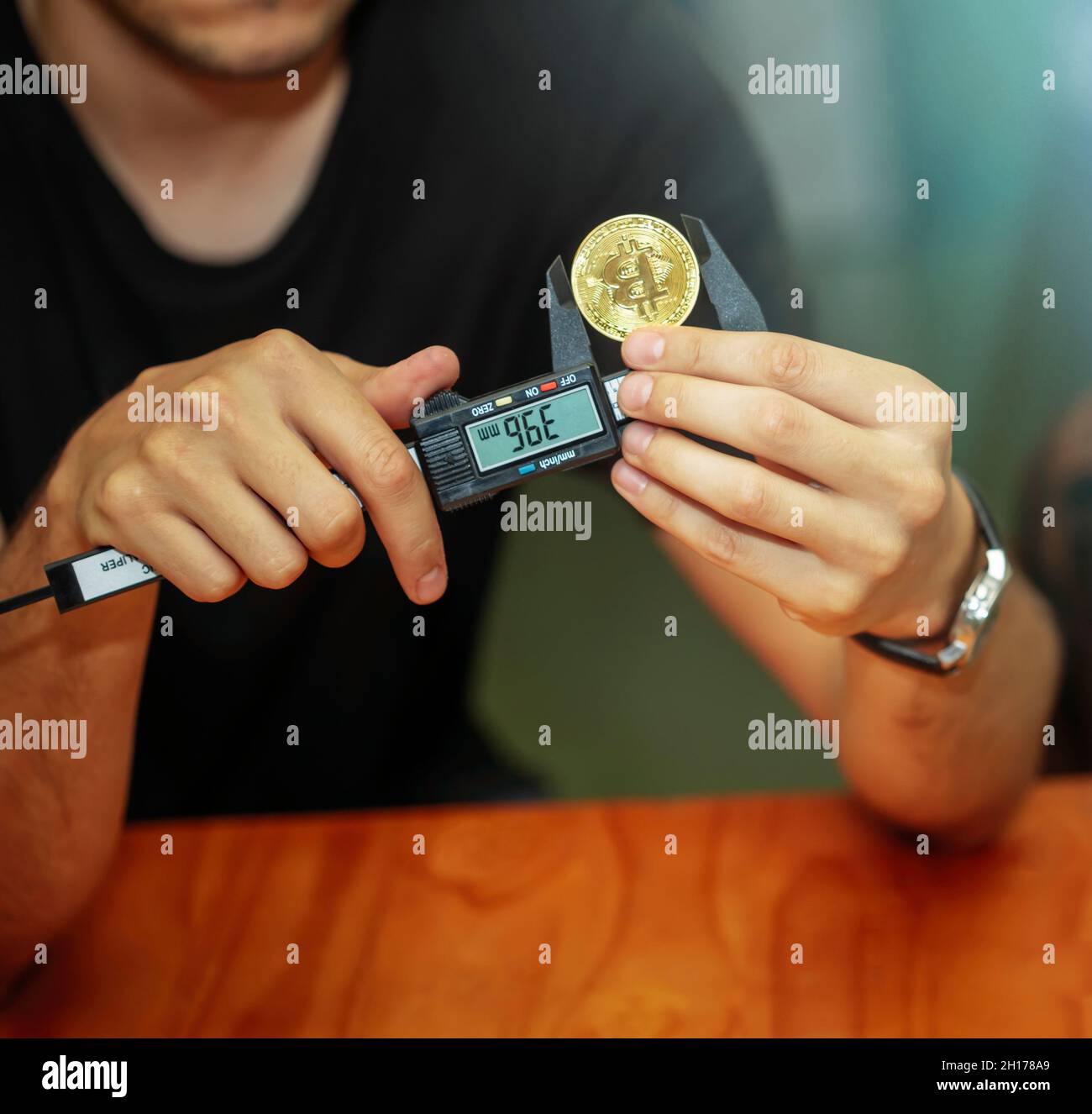 Junger Mann, der mit einem Messschieber die Größe der virtuellen Bitcoin-Währung misst Stockfoto