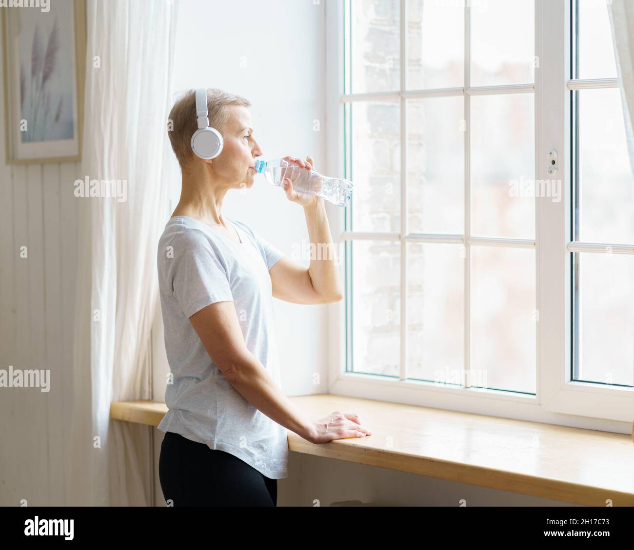 Glückliche ältere Frau, die nach dem Sporttraining Wasser aus der Plastikflasche trinkt Stockfoto