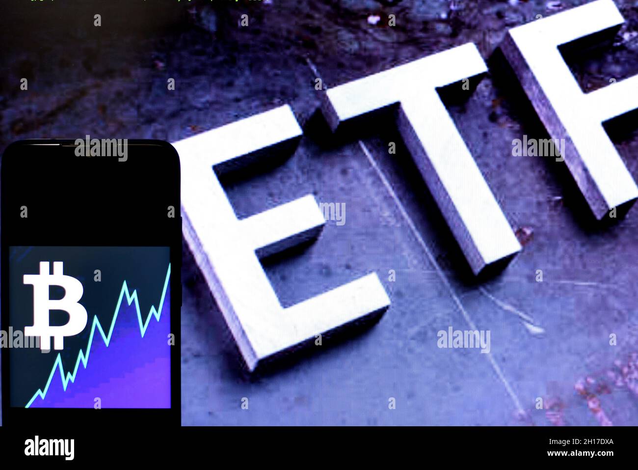 In dieser Fotolabbildung wird ein Bitcoin-Logo auf einem Smartphone mit einem ETF-Logo (Exchange Traded Fund) im Hintergrund angezeigt Stockfoto