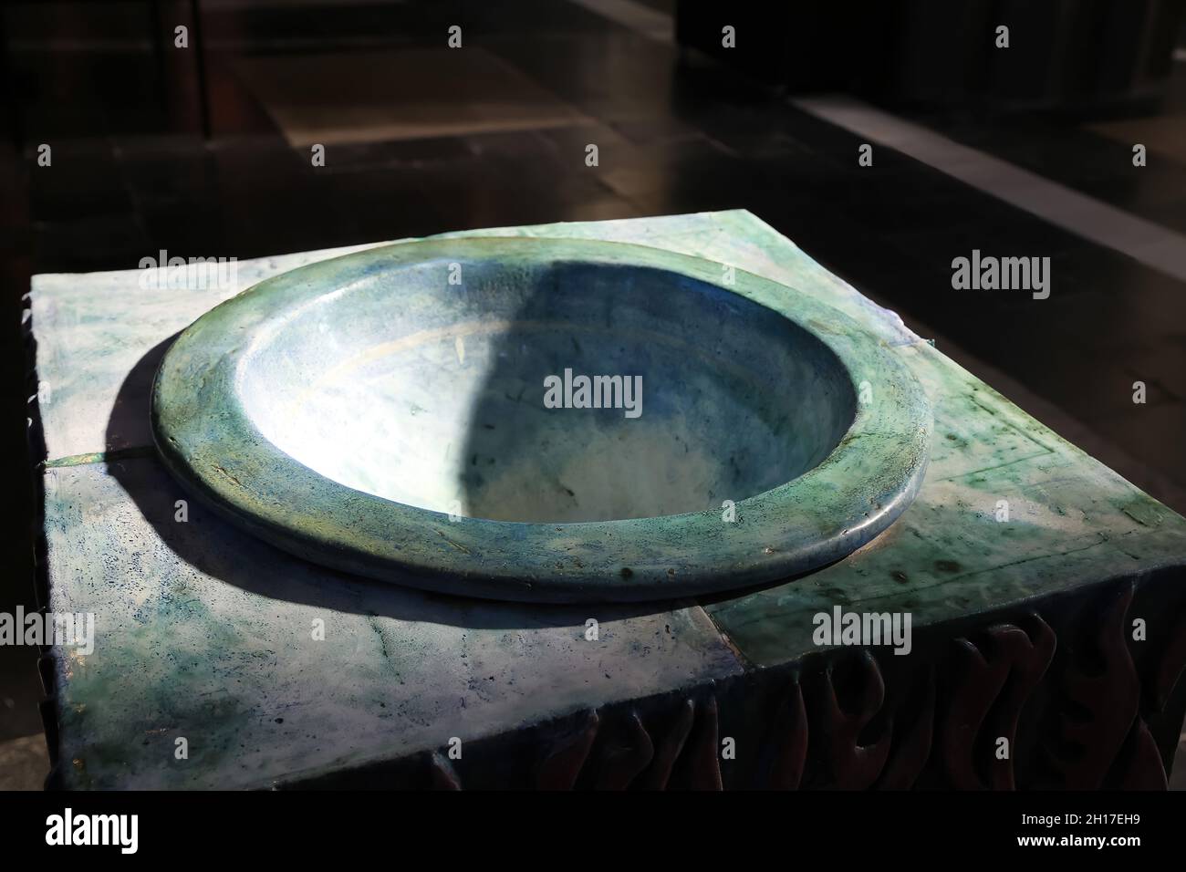 Blick auf ein isoliertes, grün-blaues, altes mittelalterliches Taufbecken aus Marmor, das von natürlichem Sonnenlicht in der katholischen Kirche - Brügge, Belgien, beleuchtet wird Stockfoto