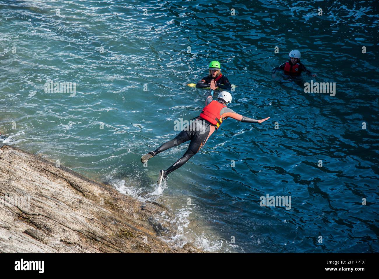 Urlauber, die mit ihrem kolenkenden Fremdenführer an der Küste von Towan Head in Newquay in Cornwall ins Meer springen. Stockfoto