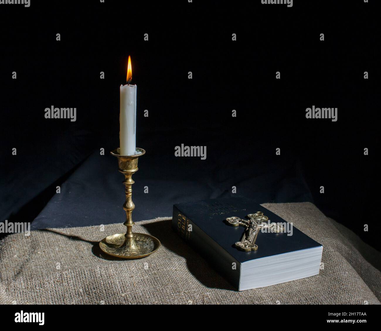 Bronzekreuz, brennende Kerze und bibel auf dem Tisch in der Nähe Stockfoto