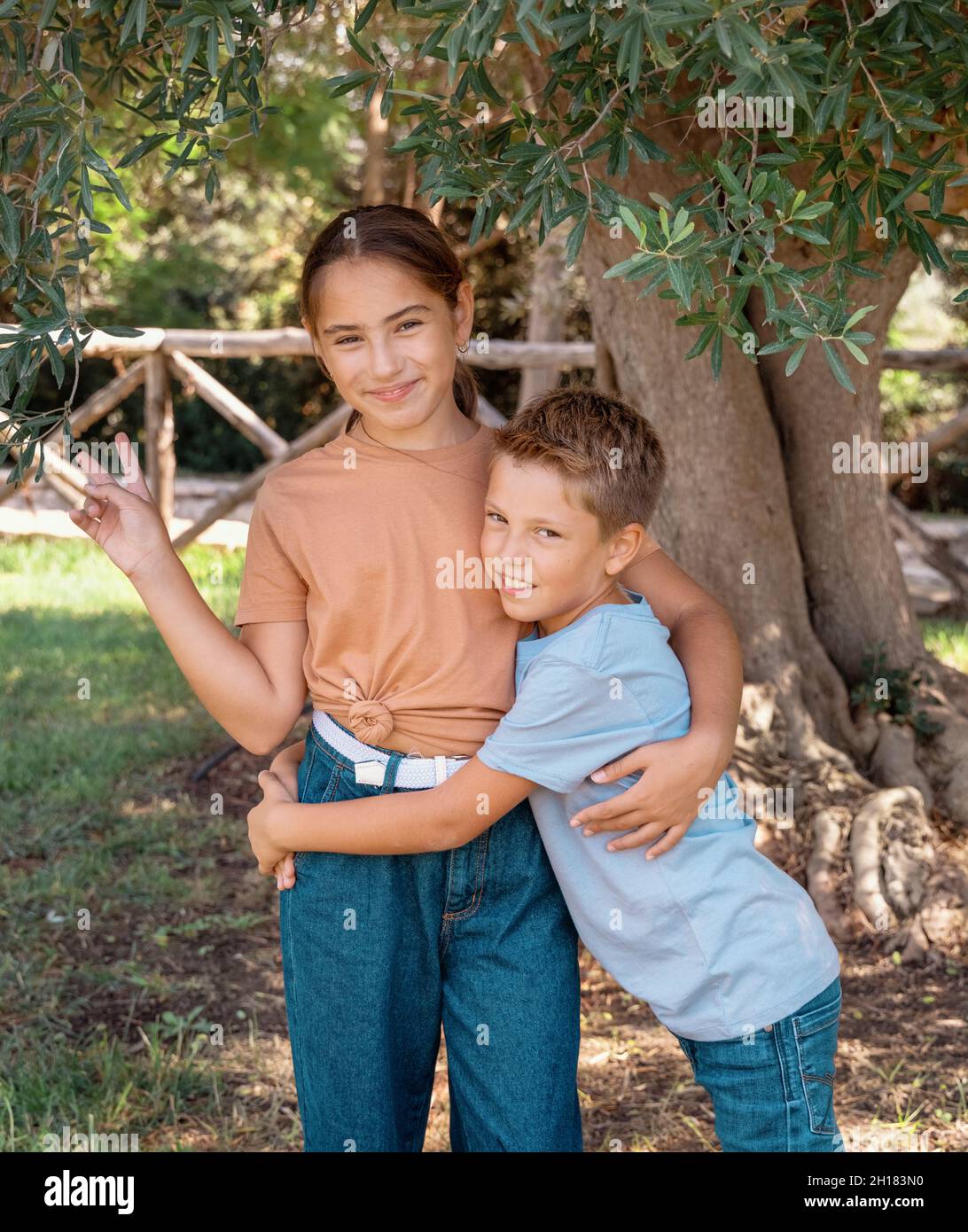 Fröhlicher Bruder und Schwester umarmen sich gegenseitig und zeigen V gest im Freien. Nettes Kind Mädchen und Junge Spaß in einem Park im Sommer. T-Shirt-Modell Stockfoto
