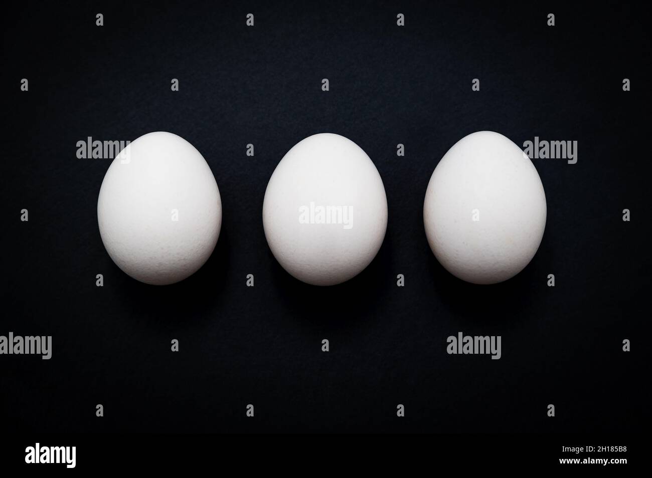 Horizontales Frühstück, dreifach: Drei weiße Hühnereier vor dunklem Schiefergrund. Stockfoto