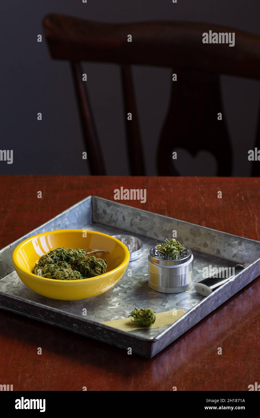 Medizinische Marihuanaknospen oder Hanfblumen mit Kräuterschleifer und Rauchzubehör in Metalltablett auf Holztisch Stockfoto