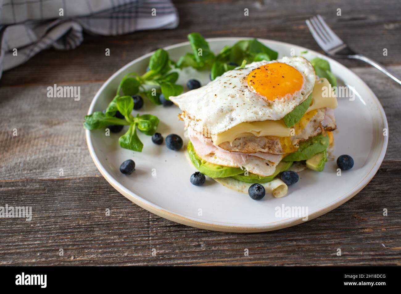 Ketogenisches Frühstück mit Spiegeleiern, Sonnenseite oben, mit Schinken, Käse und Avocado. Serviert mit frischen Heidelbeeren und Lammsalat´s einem Teller. Stockfoto
