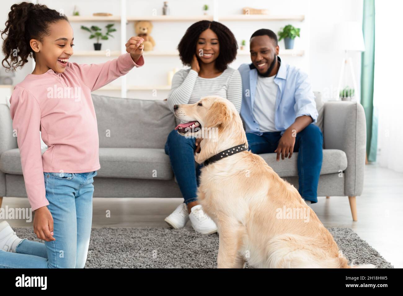 Happy black girl giving treat to her labrador Stockfoto