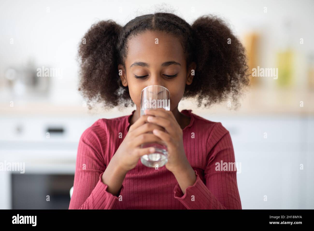 Ziemlich schwarzes Mädchen Trinkwasser, Küche Innenraum Stockfoto