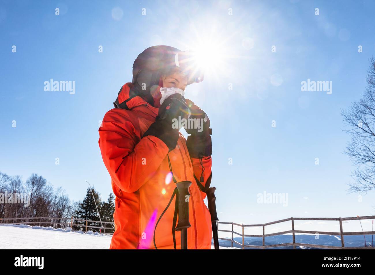 Wintersport-Frau Skifahrerin bläst ihre Laufnase beim Skifahren auf Bergskipiste im Freien. Asiatische Athlet Mädchen trägt Helm und Handschuhe, Jacke Stockfoto