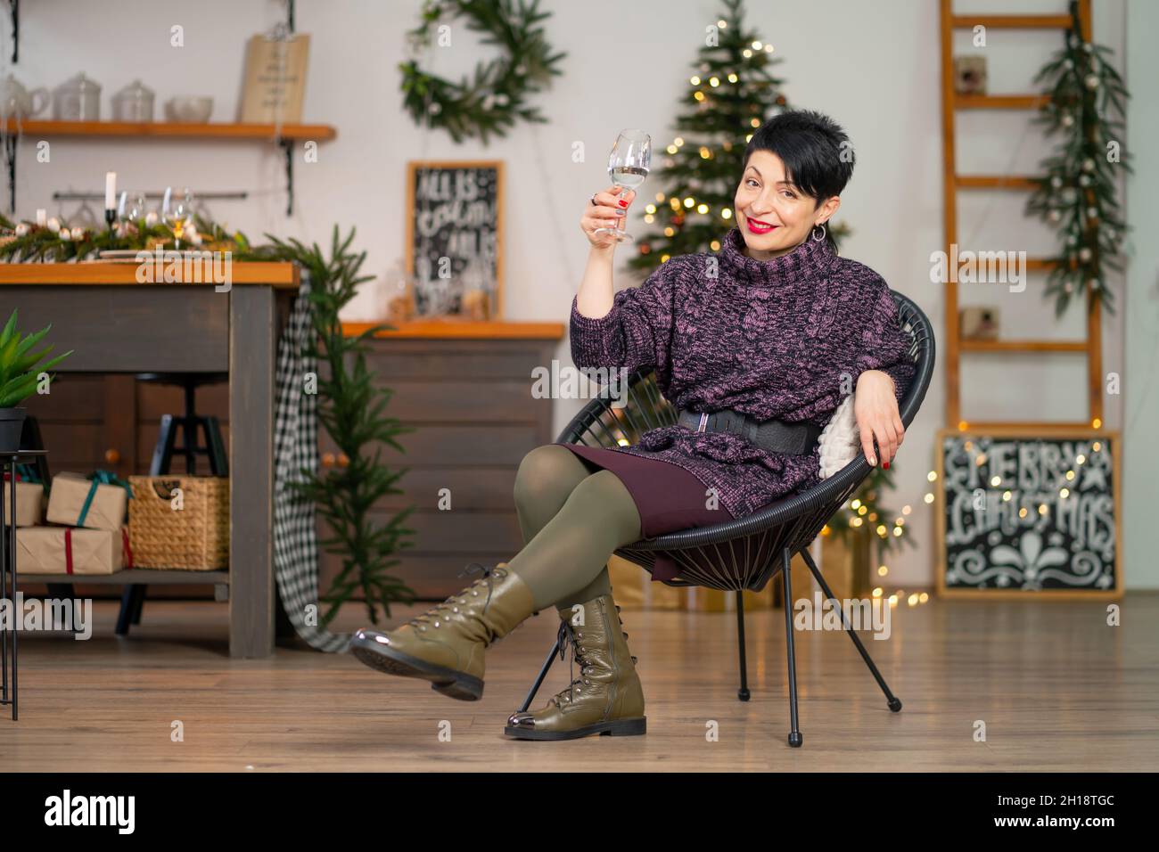 Kurze Haare Brünette Frau mit einem Glas Champagner sitzt auf einem Stuhl Weihnachten feiern. Stockfoto
