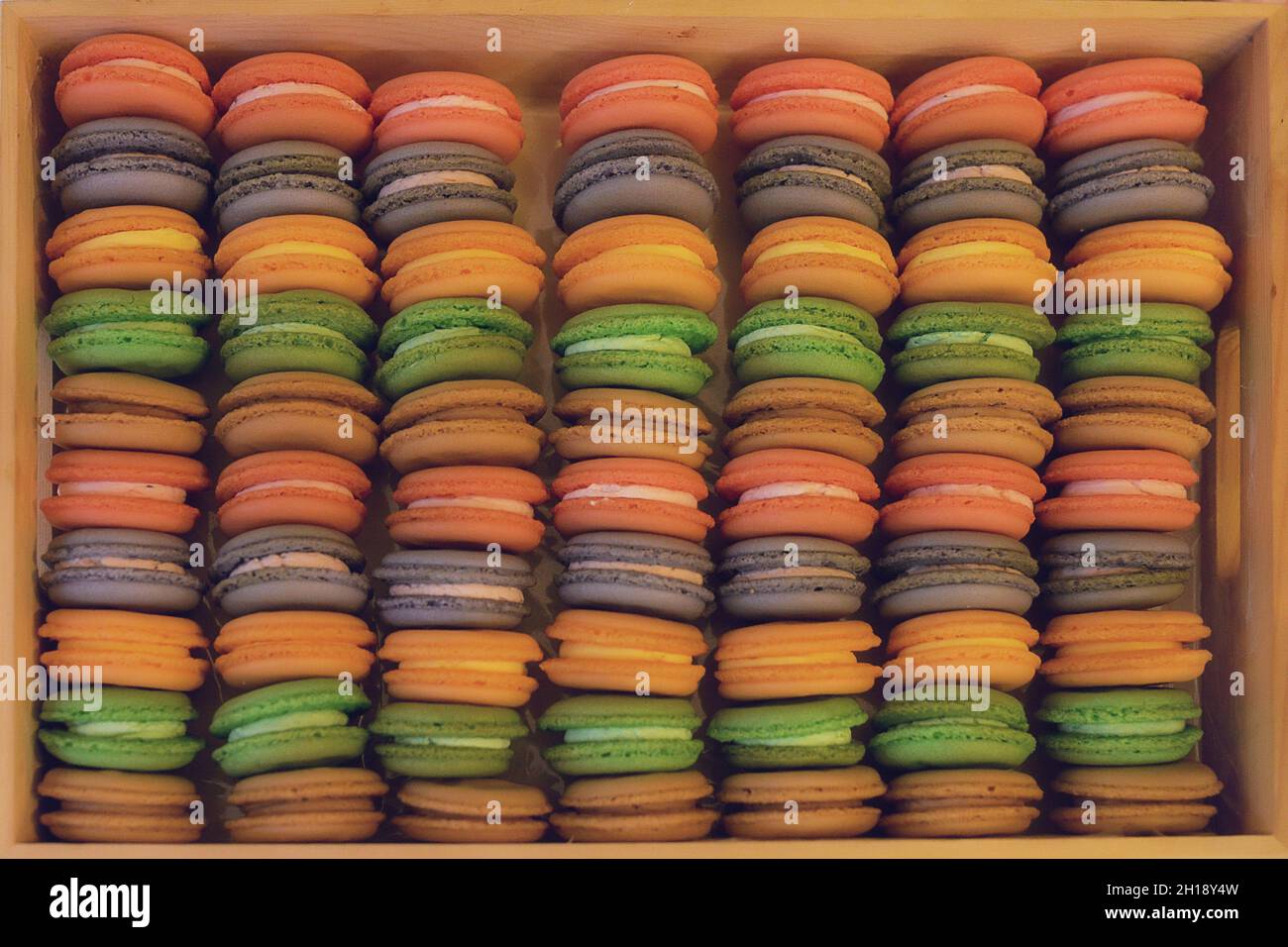 Pastellmakarons, farbenfrohe Lebensmittelhintergrund, wiederholtes Muster beliebter französischer Süßwaren in einer Holzkiste mit weichem Warmlichtfilter Stockfoto