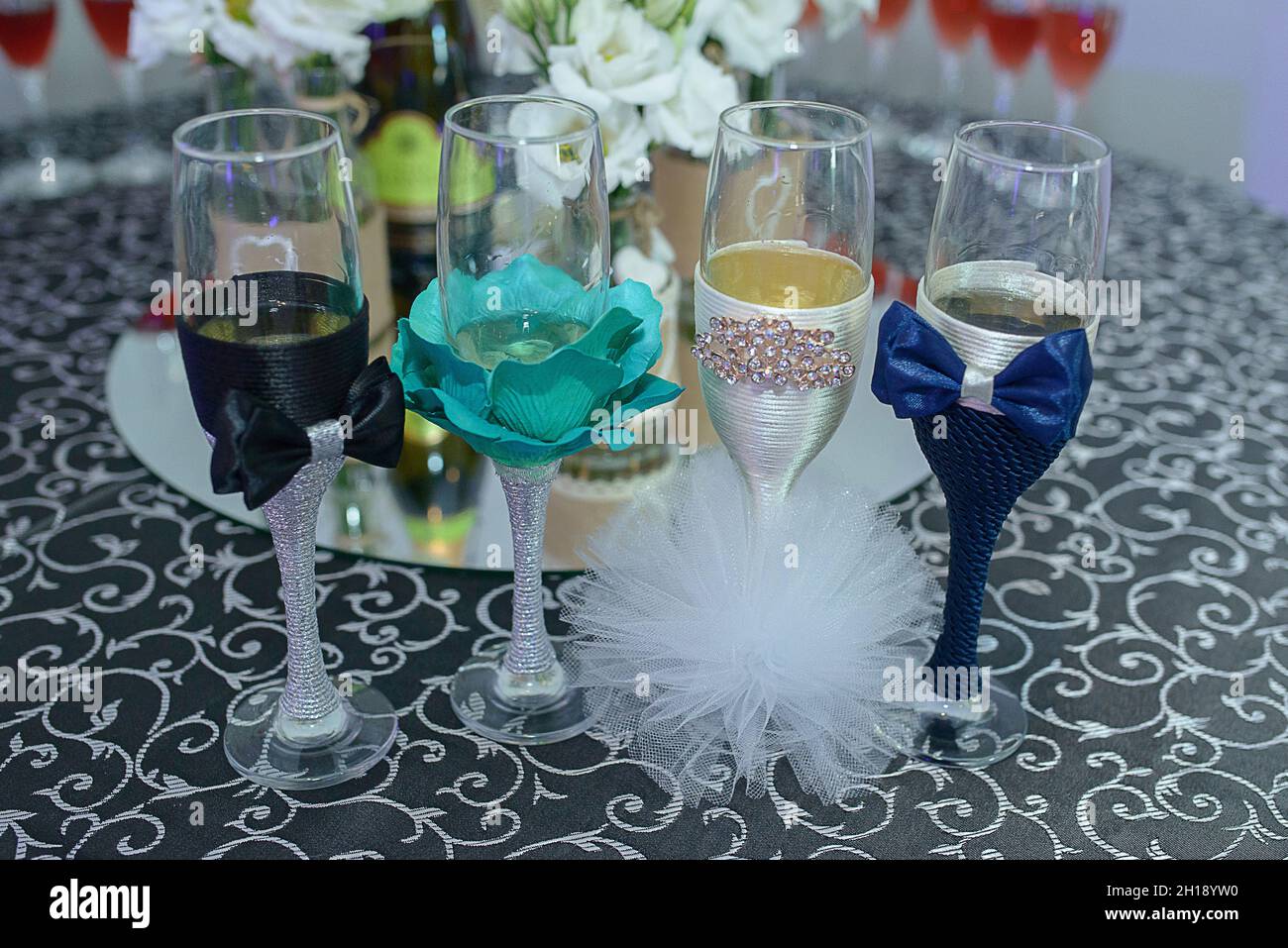 Vier spielerisch dekorierte Flötengläser für eine Hochzeit, mit Fliege und Bommel-Poms, die den Braut- und Bräutigam-Outfits ähneln, niedliche Gläser für Gäste-Drinks Stockfoto