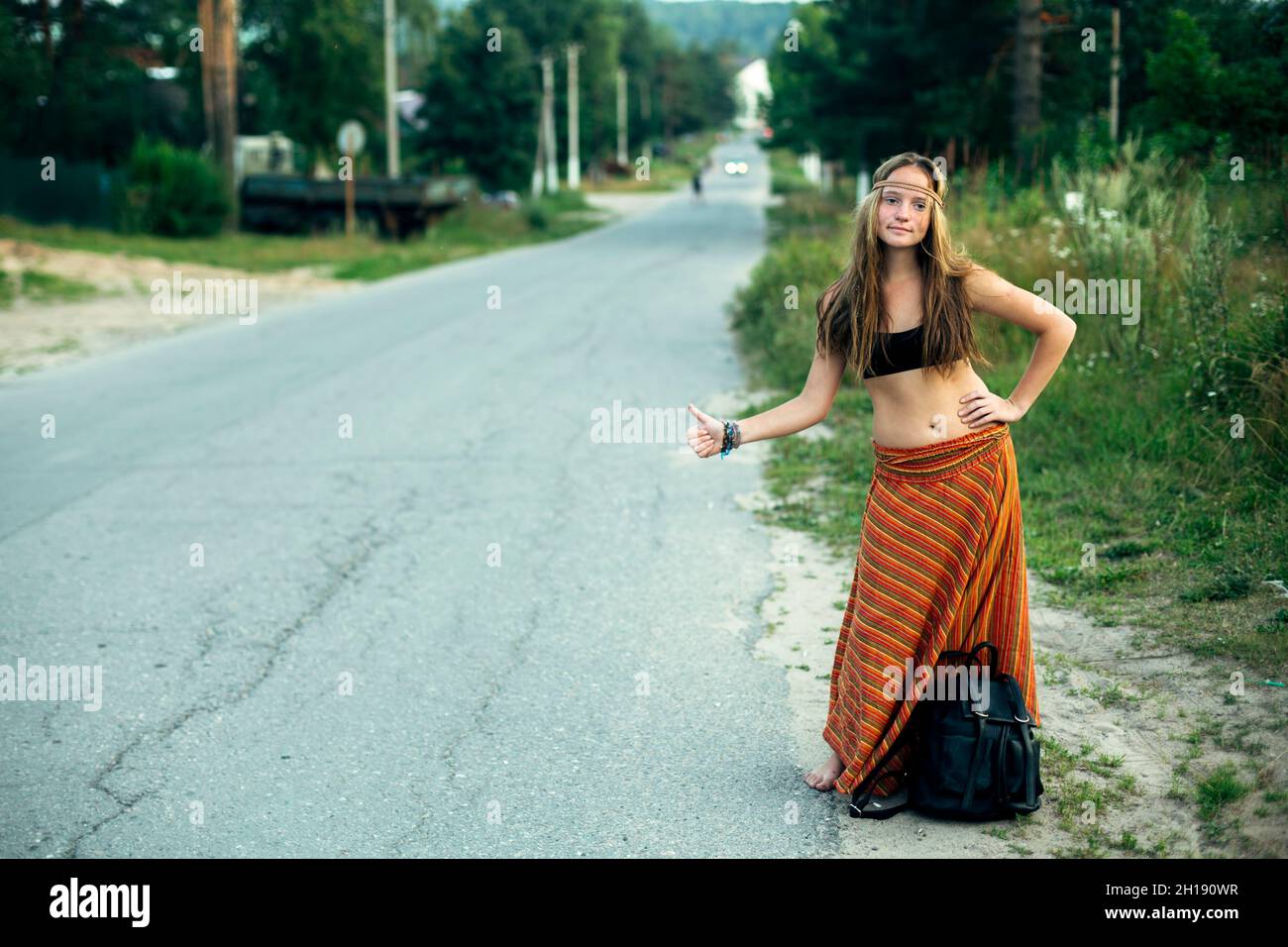 Ein Hippie-Mädchen, das in der Nähe der Landstraße stimmt. Anhalter für Wanderungen. Stockfoto