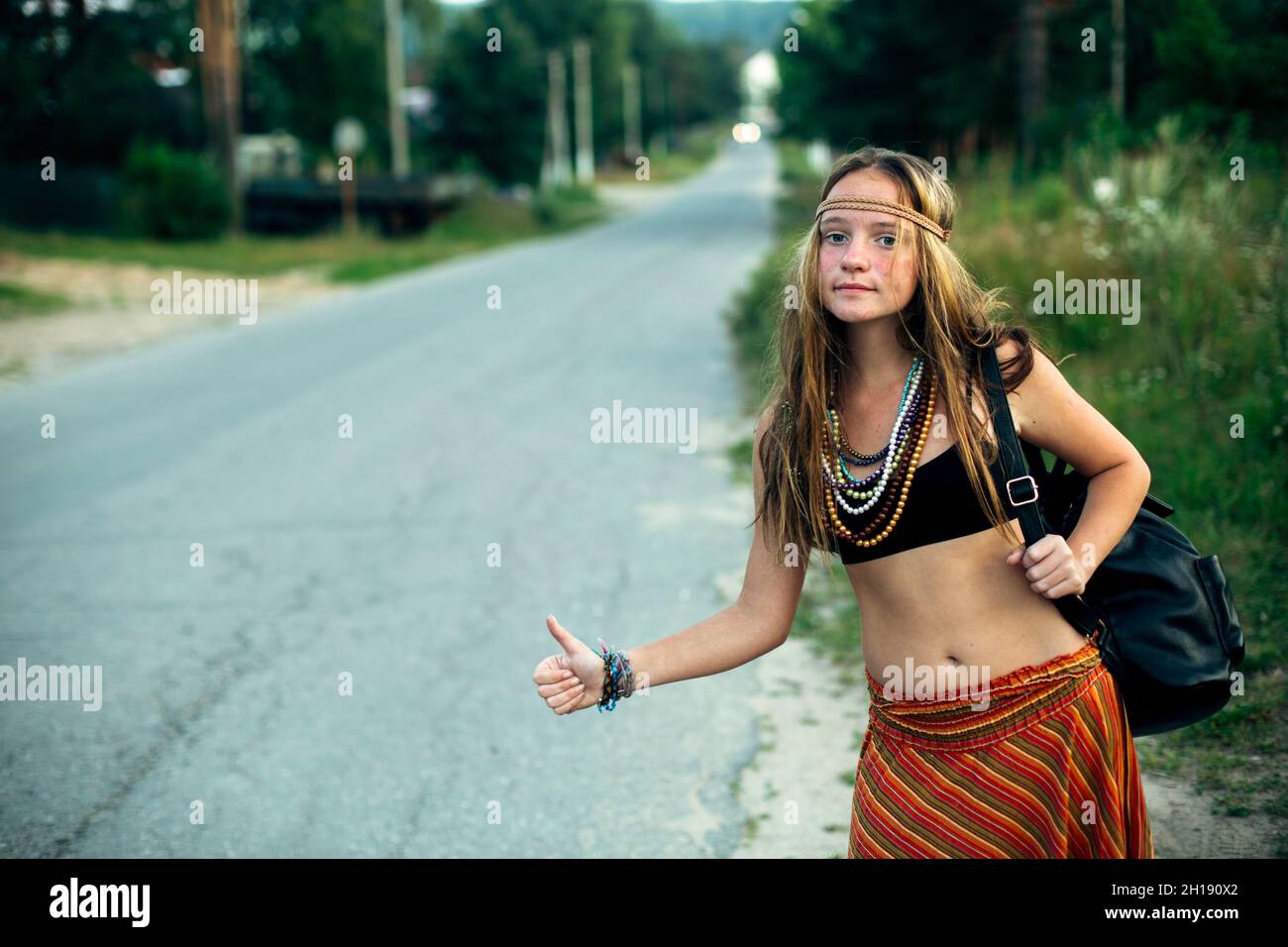 Hippie-Mädchen, das in der Nähe der Landstraße stimmt. Anhalter. Stockfoto