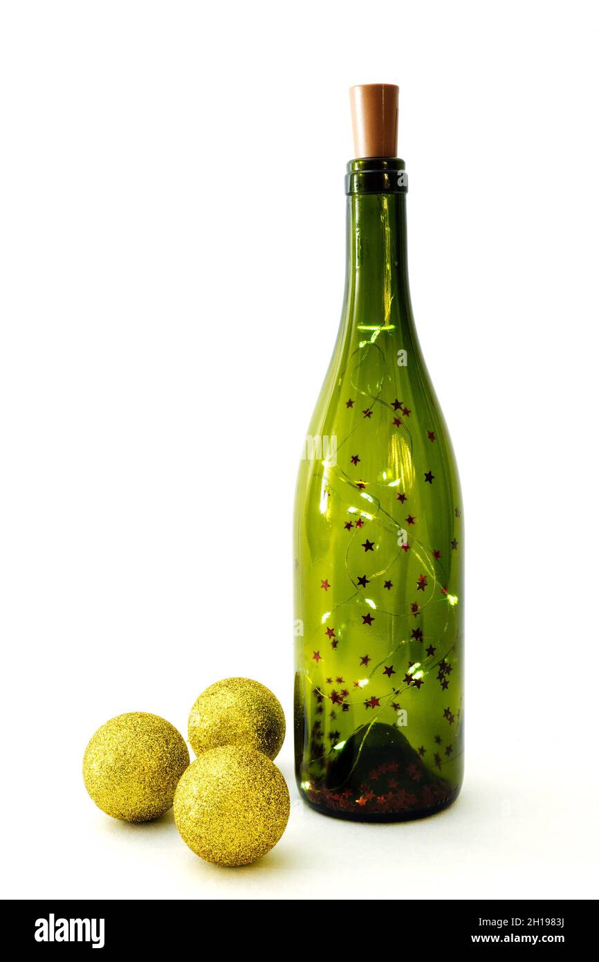 Girlande in Glasflasche für Wein und drei goldglänzende weihnachtskugeln auf weißem Hintergrund. Selektiver Fokus, vertikale Ansicht Stockfoto