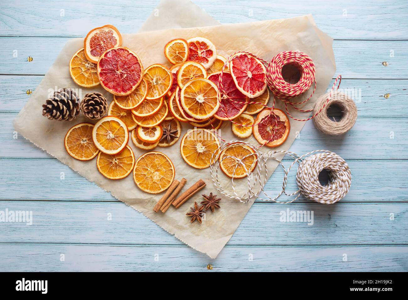 Zimt, Anis, getrocknete Orangen und Grapefruitscheiben, Fäden für diy-Projekte, Geschenkverpackung und schöne Öko-Weihnachtsdekorationen wie Kränze auf einem blauen Holztisch angeordnet Stockfoto