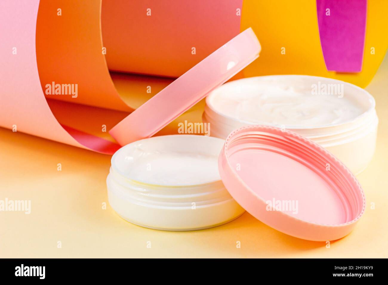 Weißer Kunststoff-Kosmetikbehälter für feuchtigkeitsspendende Creme als Nachbildung auf hellem rosa, orangen und gelben Hintergrund. Körper- und Hautpflege, Gesundheit, Wellnes Stockfoto