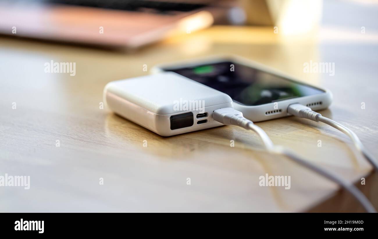 Ein Smartphone wird von einer kleinen weißen Powerbank geladen. Stockfoto
