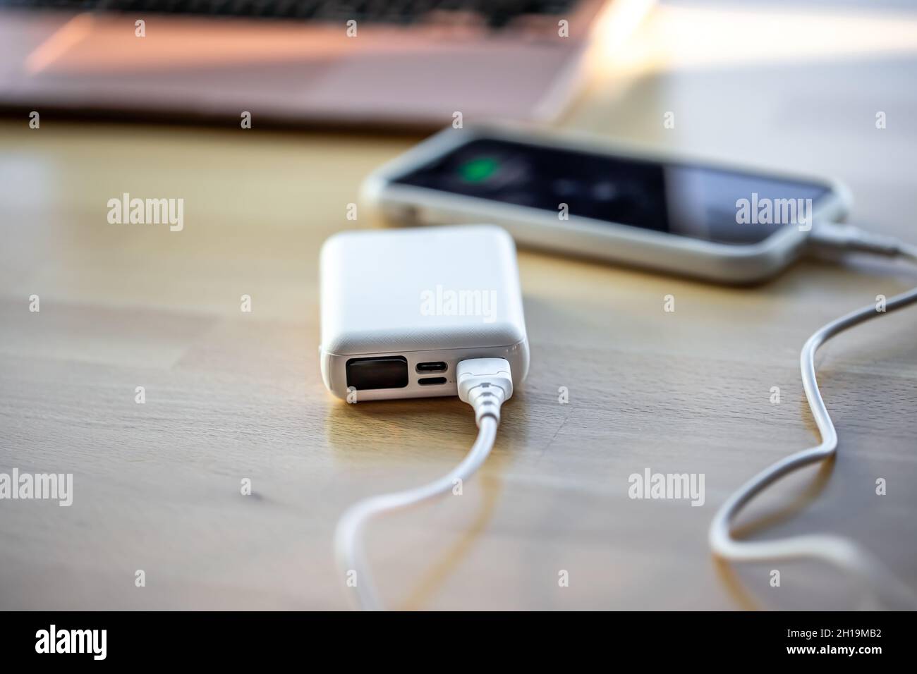 Ein Smartphone wird von einer kleinen weißen Powerbank geladen. Stockfoto