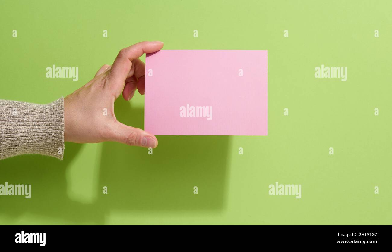 Weibliche Hand hält leeres rosa Papier auf grünem Hintergrund. Kopieren Bild oder Text einfügen, Nahaufnahme Stockfoto