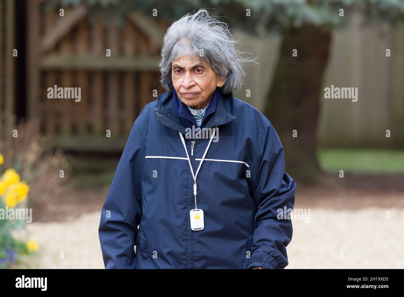 Ältere asiatische indische Frau, die im Winter im Freien geht, Großbritannien. Tragen Sie warme Kleidung und einen SOS-Anhänger mit persönlichem Sicherheitsalarm Stockfoto