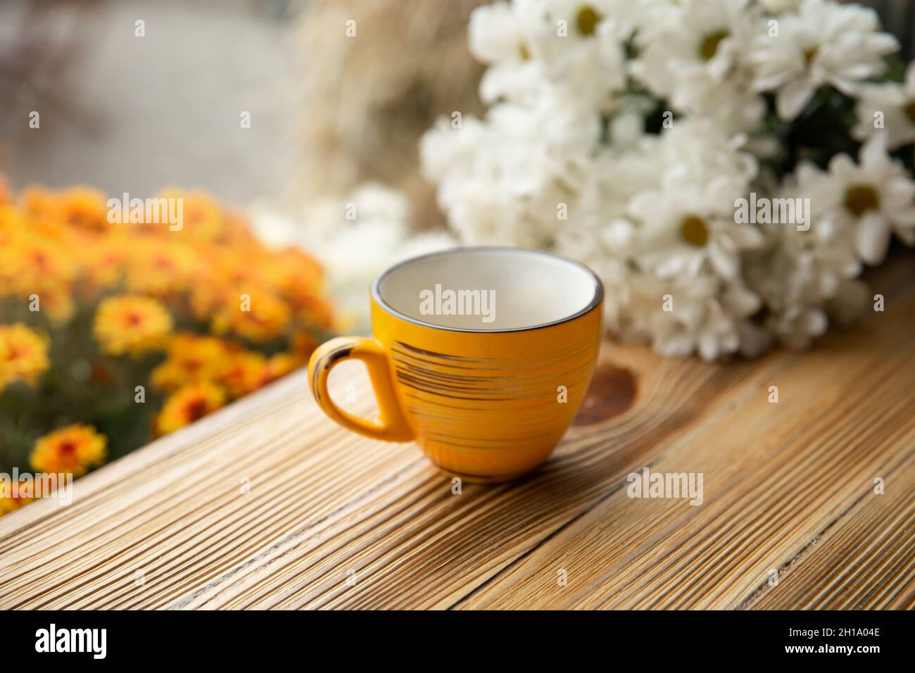 Gelbe Tasse auf einer Holzoberfläche auf einem verschwommenen Hintergrund mit Blumen. Stockfoto