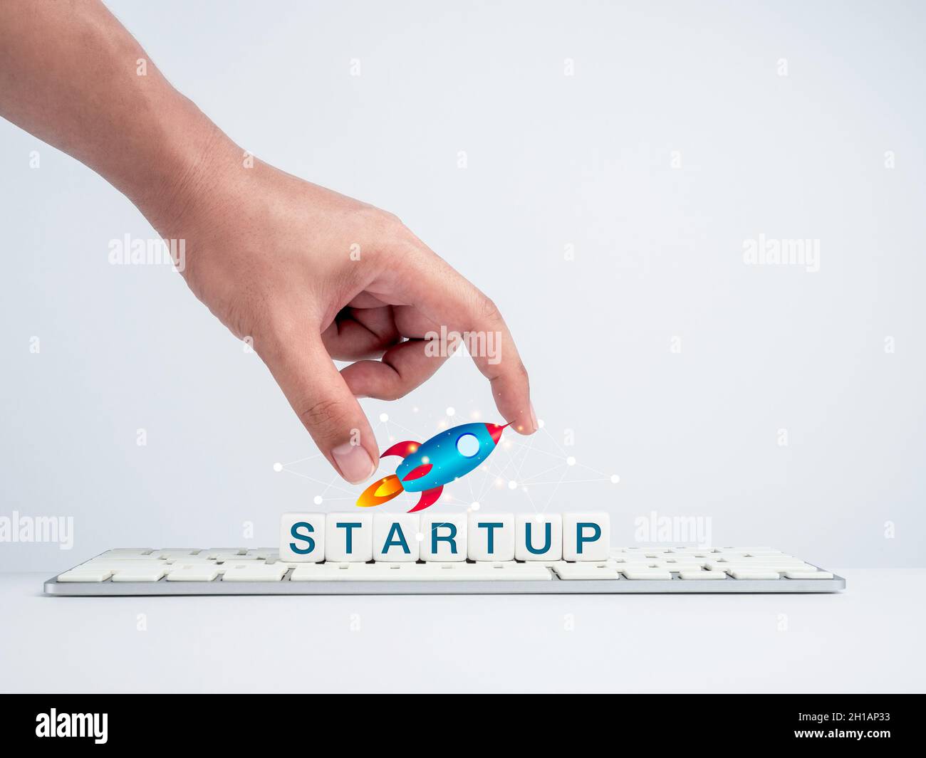 Startup-Konzept. Hand hält Rakete auf weißen Würfel Blöcke mit dem Wort, Start auf Tastatur-Computer auf einem weißen Schreibtisch und weißem Hintergrund. Success cr Stockfoto
