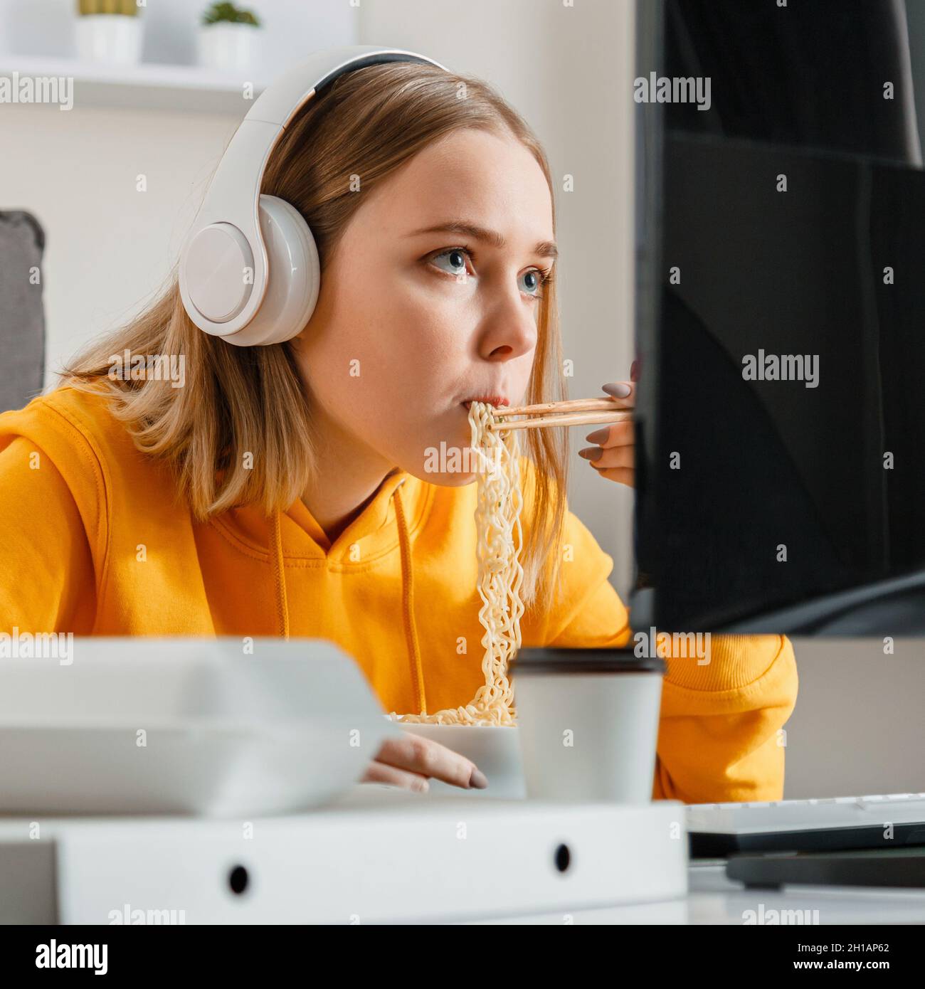 Hungrige weibliche Gamer isst Nudeln Chinesisches Gericht mit Essstäbchen im Inneren des Hauses mit Desktop-pc-Computer während des Streamings Videospiel. Teenager Stockfoto