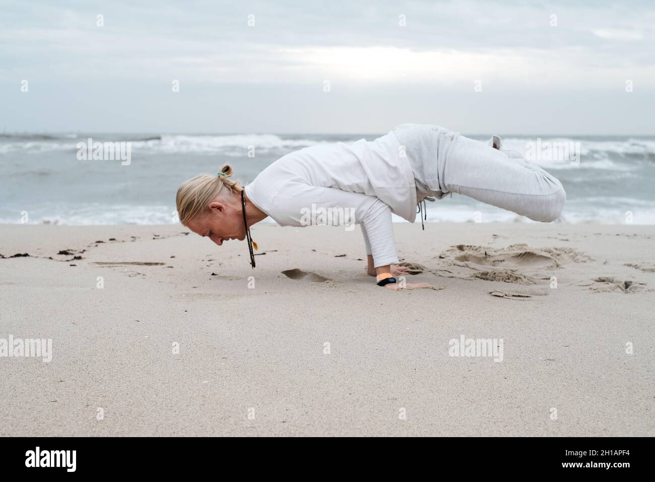 Mann macht Yoga am Strand im Herbst über Wellen im Meer. Cremig, leichter Sand und Himmel, Asanas und Meditation, Gleichgewicht im Leben, Selbstbewusstsein und Stockfoto