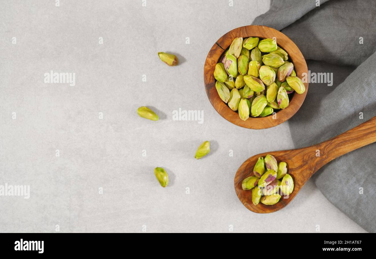 Pistazien-Nüsse in einer rustikalen Holzschale und andere Pistazien auf einem Holzlöffel Draufsicht über Schuss auf hellgrauem Tisch auf Hintergrund-Banner mit CO Stockfoto