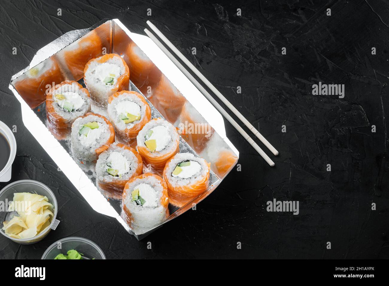 Leckere Sushi-Rollen im Einwegkartons-Set, auf schwarzem Stein-Hintergrund, mit Textrahmen und Platz für Text Stockfoto