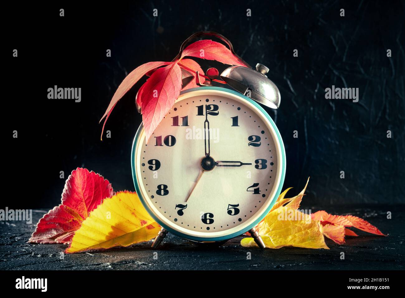 Sommerzeit-Konzept, fallen zurück im Herbst. Ein Vintage-Wecker mit Herbstlaub auf schwarzem Hintergrund Stockfoto