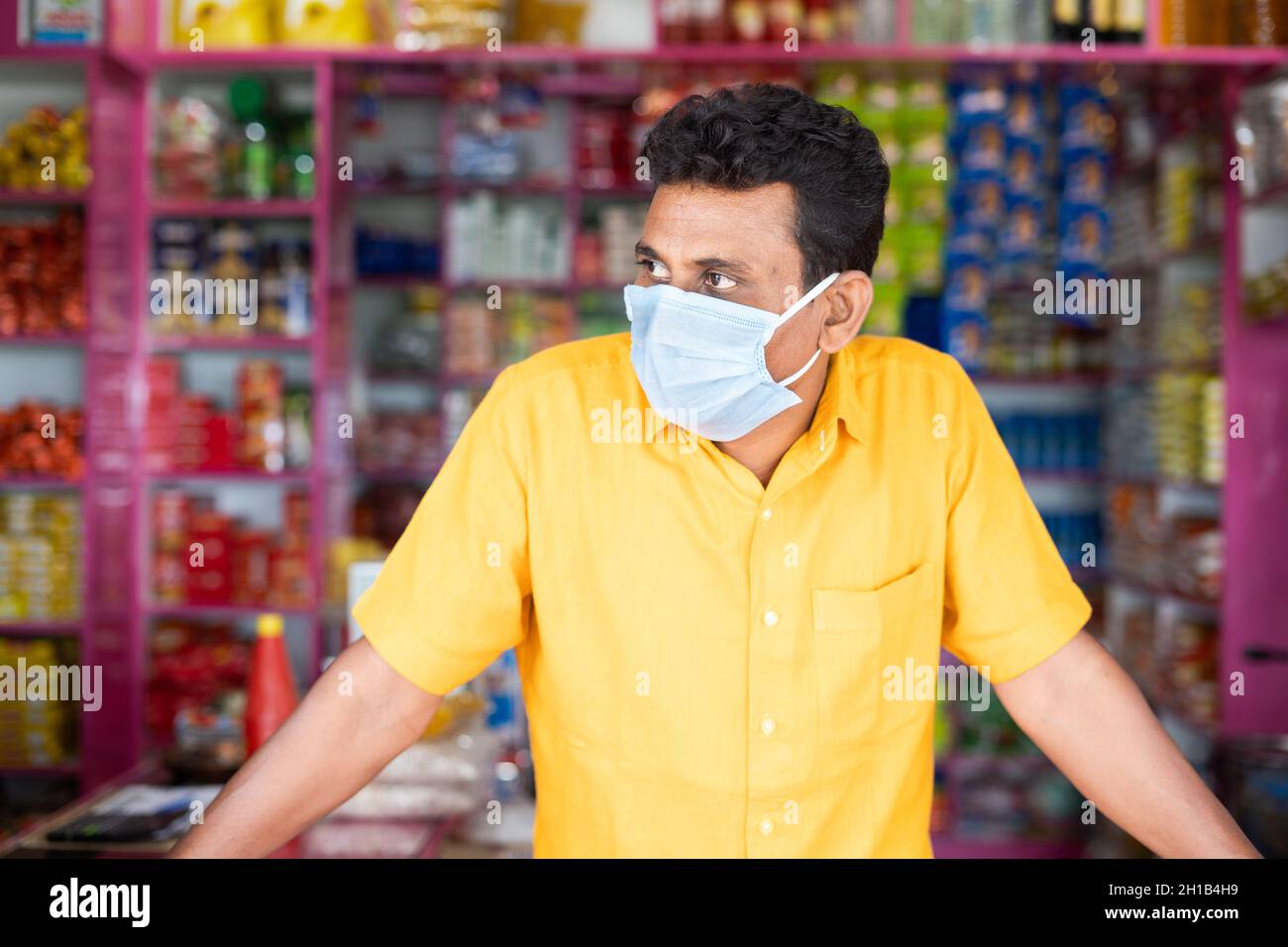 Händler mit mdical Gesichtsmaske in Lebensmittelgeschäften oder Kirana-Laden warten auf Kunden durch einen Blick auf während Coronavirus covid-19 Pandemie - Konzept der Stockfoto
