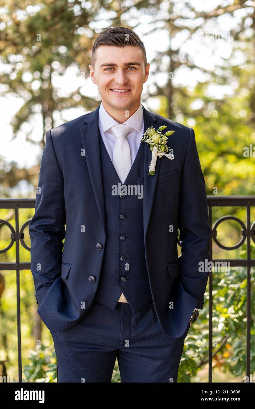 Hübscher junger Bräutigam in elegantem und stilvollem dunkelblauem Anzug im  Freien im Porträt. Fröhlicher Bräutigam, der die Kamera anschaut und  lächelt Stockfotografie - Alamy