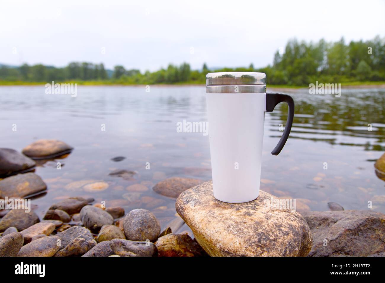Weißer Reise-Kaffeebecher mit großem Flussstein. Leerer Becher als Design-Promotion. Stockfoto