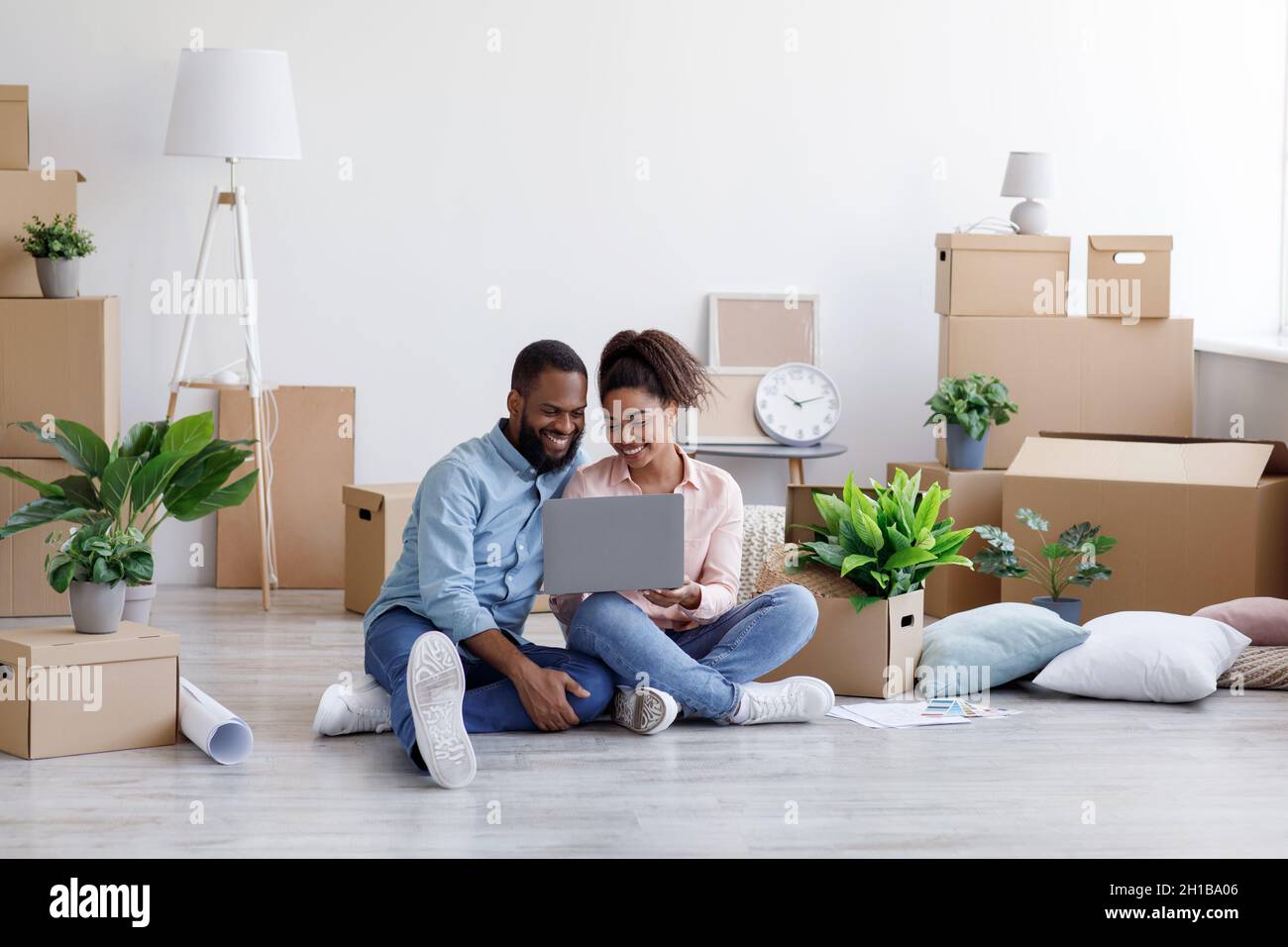 Eine frohe junge afroamerikanische Familie, die sich ausruhte und auf dem Boden zwischen Pappkartons mit Dingen saß Stockfoto