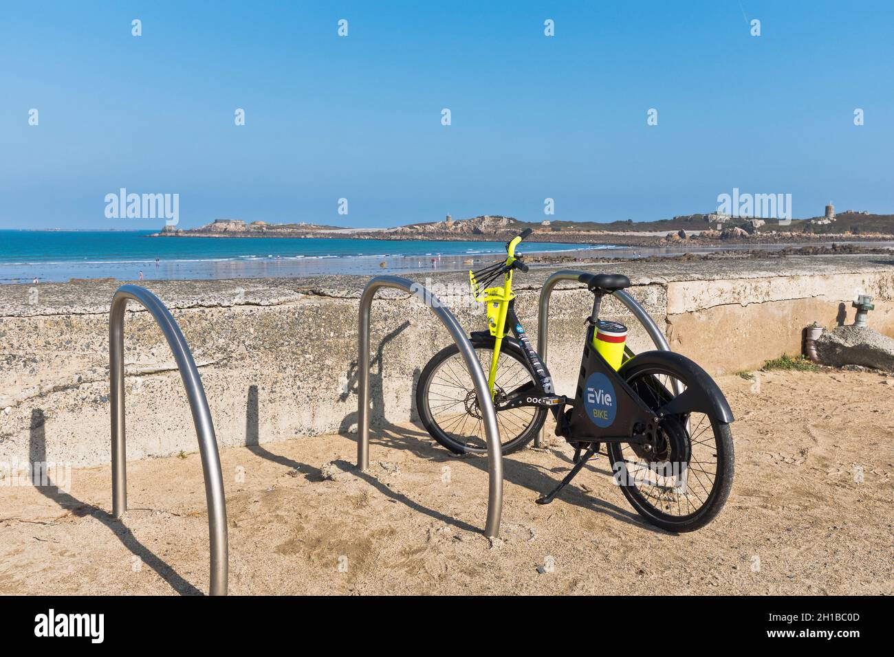 dh Evie Bike EBIKE GUERNSEY Elektrofahrräder stehen am Strand geparkt Stockfoto
