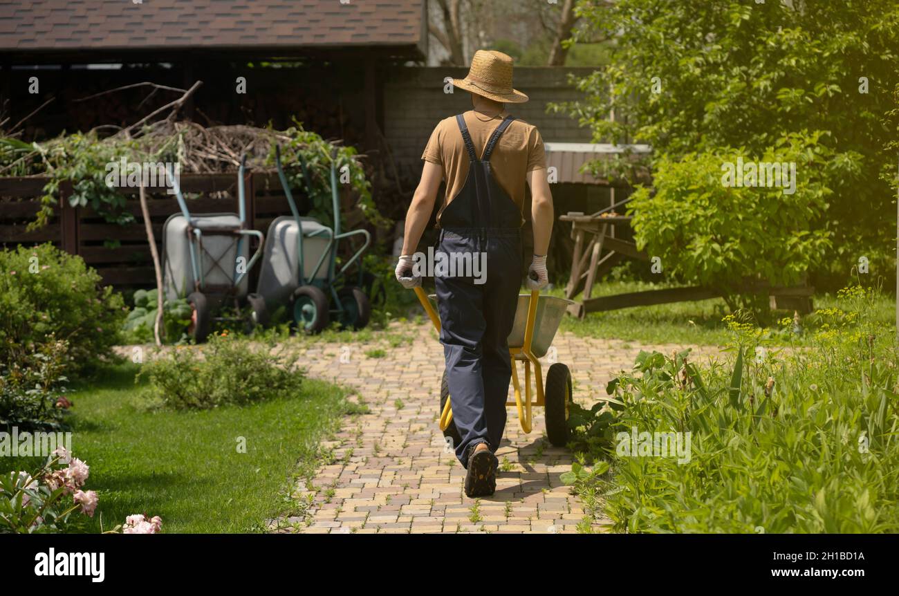 Ein junger Mann mit Händen in Handschuhen trägt einen metallenen Gartenwagen Stockfoto