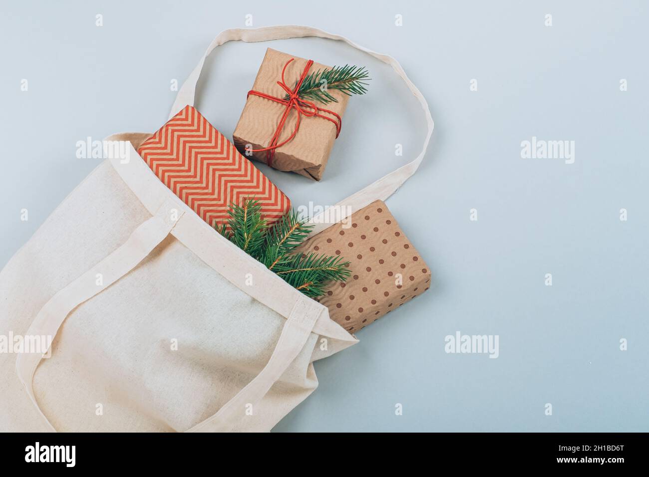 Nachhaltige Weihnachts-Geschenkschachteln in umweltfreundlicher Baumwolltasche mit Tannenzweigen, auf blauem Hintergrund. Weihnachten ohne Verschwendung. Flach liegend, Draufsicht. Hohe Qual Stockfoto
