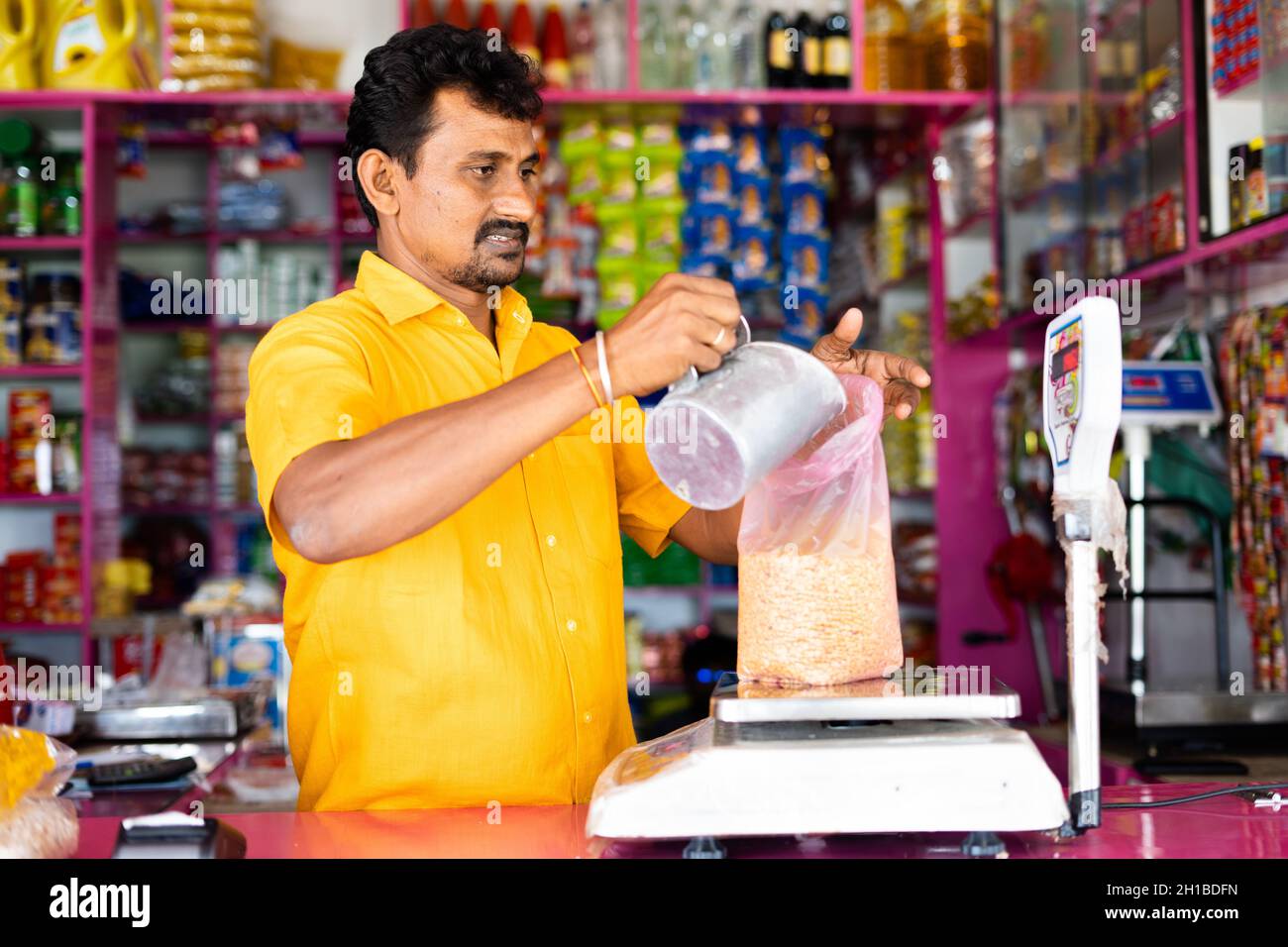 Kirana oder Lebensmittelhändler beschäftigt Messung Gewicht der Taubenerde auf Waage, bevor sie an den Kunden - Konzept der Kleinbetrieb und Beruf Stockfoto