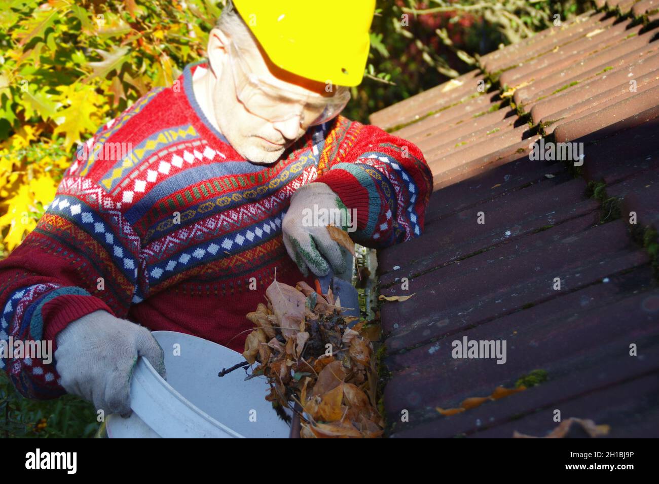 Mann, der das Dach von heruntergefallenen Blättern reinigt. Eine saubere Rinne in der Herbstsaison. Das Haus draußen halten. Hauswartung. Stockfoto