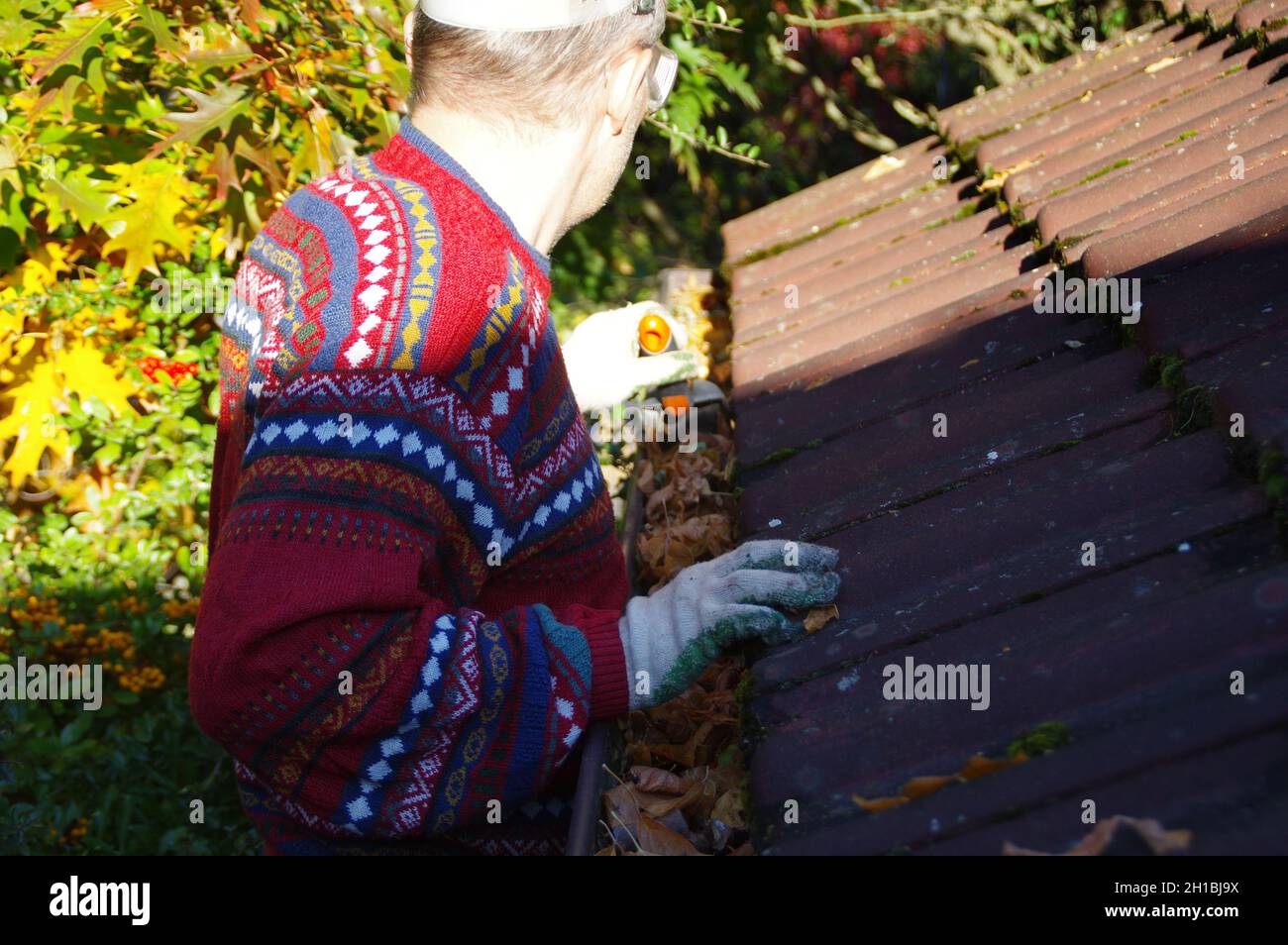 Mann, der das Dach von heruntergefallenen Blättern reinigt. Eine saubere Rinne in der Herbstsaison. Das Haus draußen halten. Hauswartung. Stockfoto