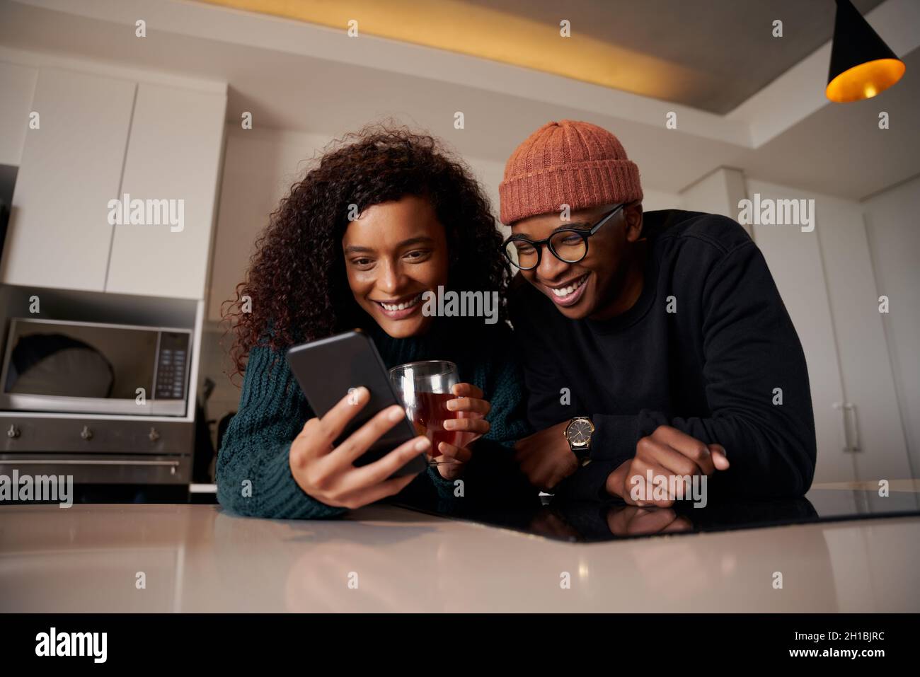 Multiethnisches Paar, das in einer modernen Wohnung in der Küche am Telefon lächelt Stockfoto