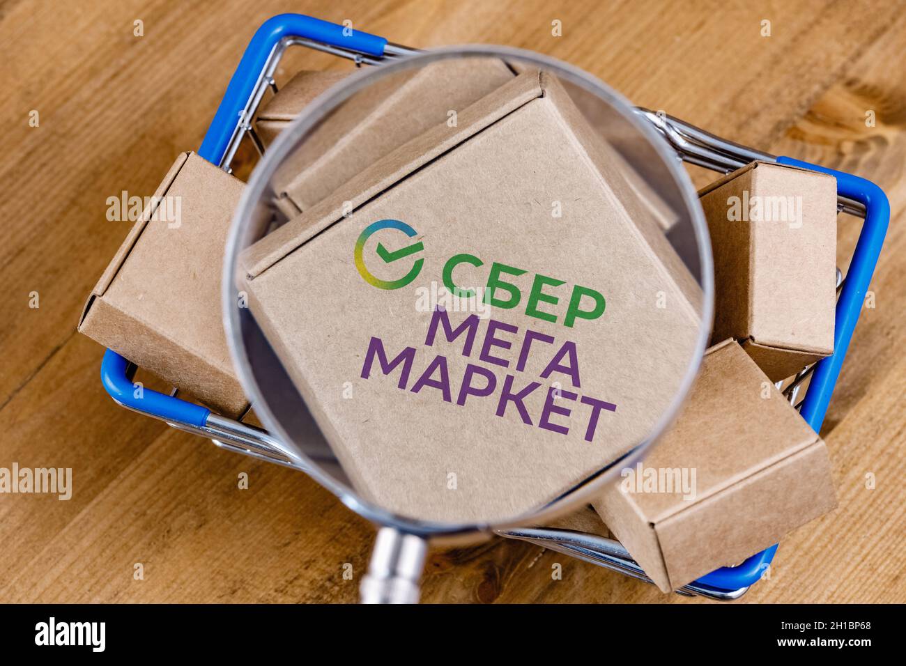 Modifizierte Aufnahme des SberMegaMarket-Logos auf einer Box unter der Lupe im Warenkorb. Stockfoto