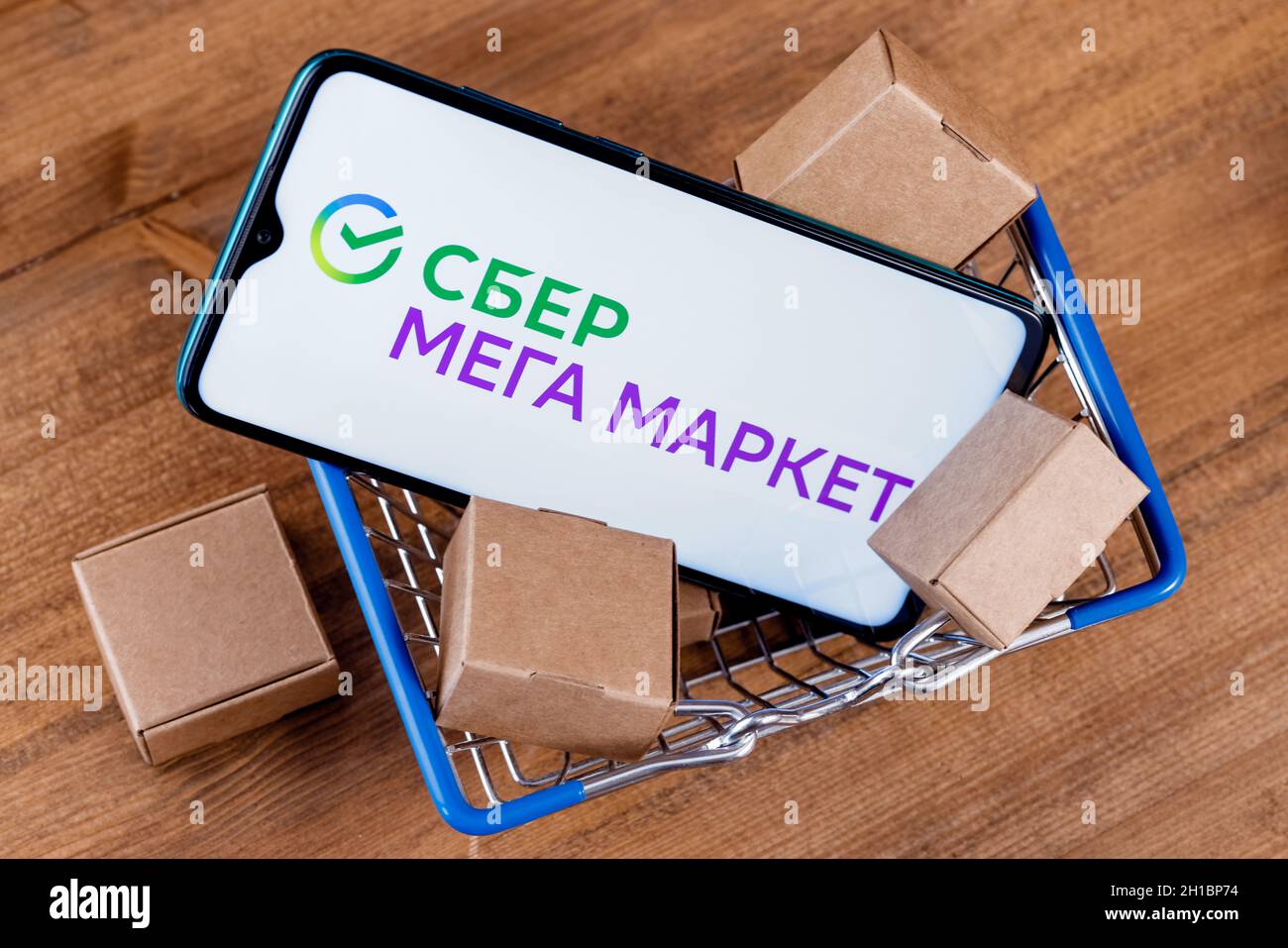 SberMegaMarket ist ein russischer Marktplatz im Besitz der Sberbank. Smartphone mit SberMegaMarket-Logo auf dem Bildschirm und Paketen im Warenkorb. Stockfoto